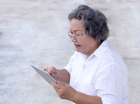 old asian grandmother watch and touch tablet on white backgroundの写真素材