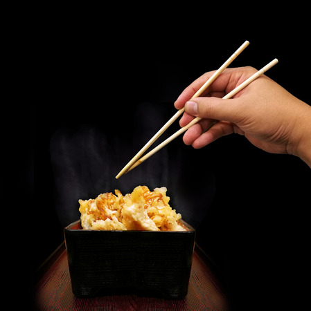 close up crispy vegetable and shrimp japaness food style call tempura in black wood box and plate with sauce and hand hold shopstick in dark conceptの写真素材