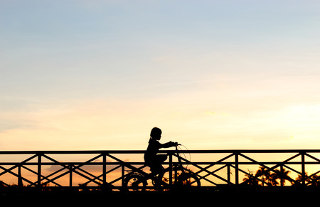 silhouette girl biker riding bicycle on the bridge in sunsetの写真素材
