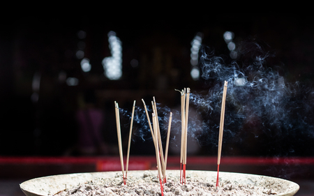 close up burning incense stick on sand box at temple in thailand with dark background and polution toxic in traditionの写真素材