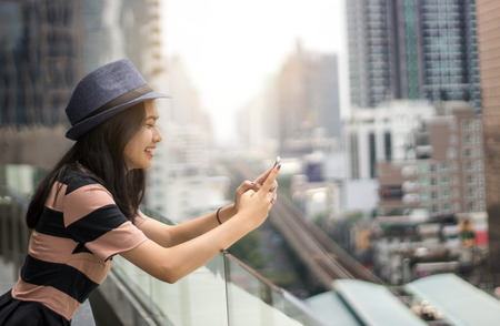 asian girl use mobile phone to chat on bacony of city scape in morning
