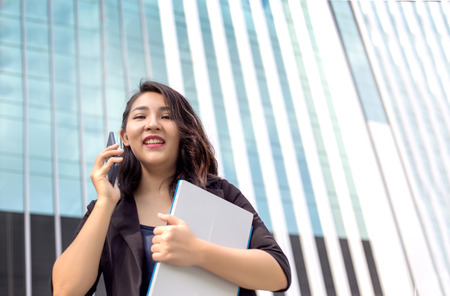 confidence smart asian business lady hold her laptop and talking front of high building in urban location action seriousの写真素材