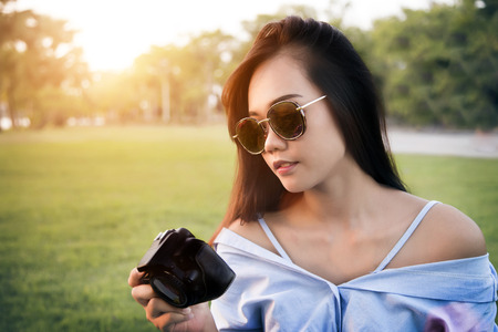 asian girl take look at digital camera in park with sunglasses