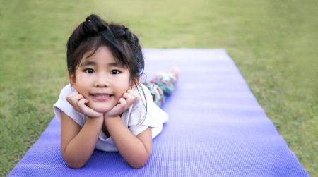 cute asian girl lie on the tummy on yoga mat and green grass  の写真素材