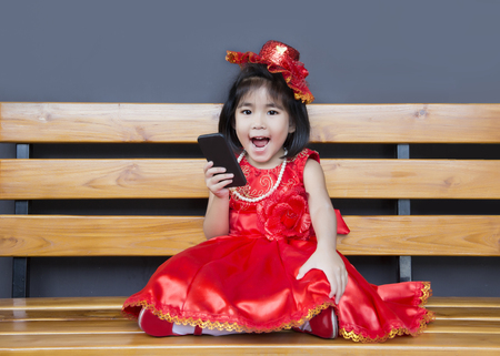 asian girl in red vintage dress use smartphone and smile to camera on wood seatの写真素材