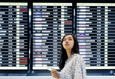 asian girl checking flight at airport tableの写真素材