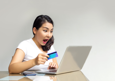 asian woman shopping on line with laptop and credit card in shock actionの写真素材