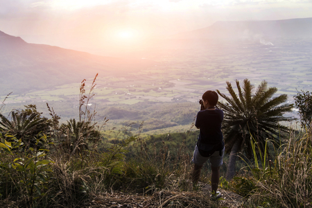Hipster young girl  taking photo of amazing landscape sunset on mountain. Tourist traveler in adventure concept.の写真素材