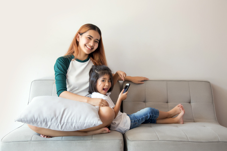Asian kids using smartphone sitting together on sofa, happy little sister holding phone enjoying mobile app with smiling sister, cute children girl having fun playing mobile.Activities in digital generation concept.の写真素材