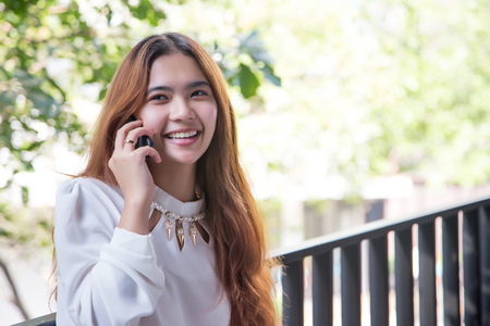Happy asian girl talking with mobile phone front of high building. digital communiation with mobile is behavior of generation in urban.の写真素材