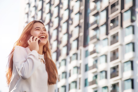 Happy asian girl talking with mobile phone front of high building. digital communiation with mobile is behavior of generation in urban.の写真素材