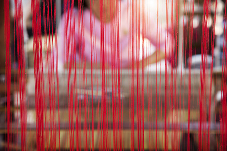 Closeup red silk string with blur human with weaving machine. Tradition textile machine with human.の写真素材