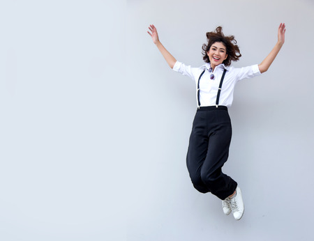 Pretty smiling joyfully asian female with curly short hair jumping action on white background, dressed hipster, being happy. Studio shot of good-looking beautiful woman and copy space.の写真素材