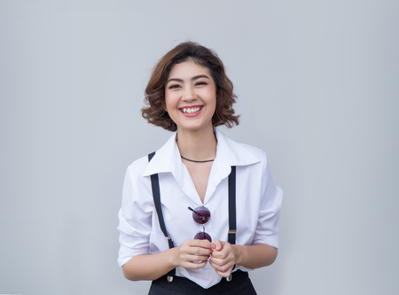 Pretty smiling joyfully asian female with curly short hair, dressed hipster, looking with satisfaction at camera, being happy. Studio shot of good-looking beautiful woman against.の写真素材