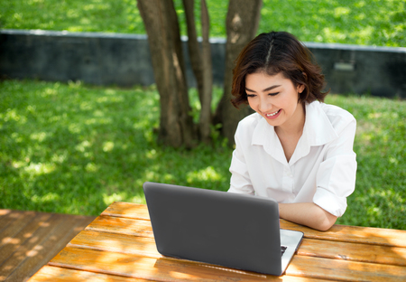 happy asian girl laughing and pointing on laptop screen on outdoor environtment in morning. People behavior with communication or shopping in digital concept.の写真素材