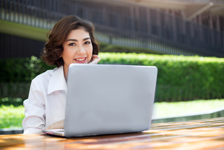 happy asian girl laughing and pointing on laptop screen on outdoor environtment in morning. People behavior with communication or shopping in digital concept.の写真素材