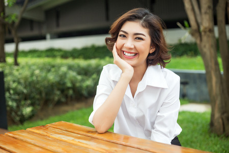 big smile face from attractive asian lady sitting on wood table. Happy people action with healthy face with good environtment. fresh air relax concept.の写真素材