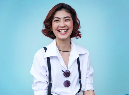 attractive smiling face of asian lady portrait on light blue background. Girl hipster dresss with white shirt and sunglasses on screenの写真素材