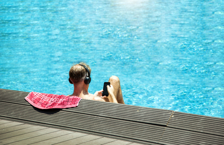 closse up head from backside with headphone relaxing near swimming pool. Man sun bath in summer and touch screen of mobile. Relax in vocation concept.の写真素材