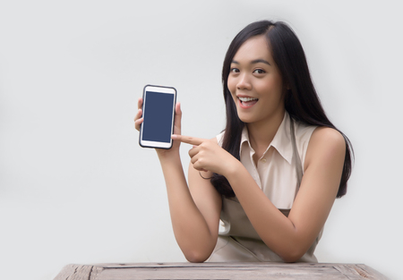 asian lady with apron dress look point at mobile screen for learning about service online with application on white backgroundの写真素材