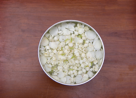 aroma water with jasmine flower in silver bolw on wood table background from top viewの写真素材