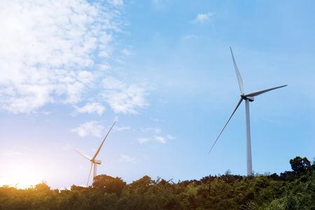 spinning wind turbine on hill with tree and blue sky. Clean energy conceptの写真素材