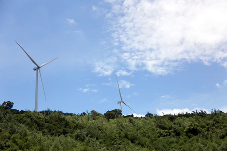spinning wind turbine on hill with tree and blue sky. Clean energy concept