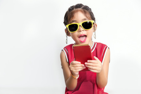 asian kid with sport shirt and sun glasses fashion funny action with mobile phone on white background, digital generation conceptの写真素材