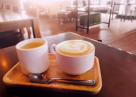 latte heart coffee and hot tea in corner of wood plate at cafe. coffee cup with copy space.の写真素材
