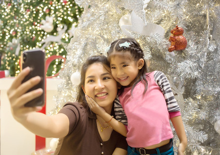 happy moment on face of asian mother and daughter hand hold mobile fot take selfie photo with Christmas tree decoration backgroundの写真素材