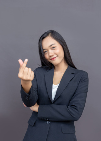 asian lady in business uniform make mini heart action by finger symbol on dark backgroundの写真素材