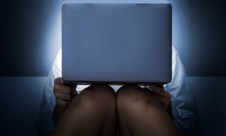 addict series online watch over clock concept. watch movies online action woth woman leg and hand sitting on bed in dark room an blue light from computer screen.の写真素材