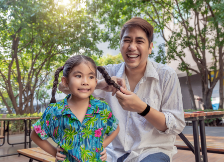stepfather concept daddy love daughter do pigtail hair for kid at park in morning. Lovely moment of...