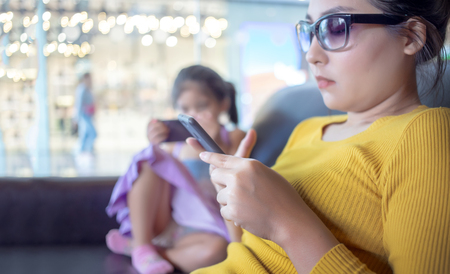 mom and kid addict mobile in digital behavior. people lost face to face relation with digital equipmentの写真素材