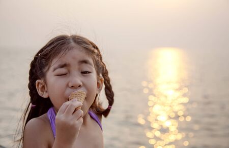 cute asian girl eating ice cream to reduce tempurature with sunset on the beach