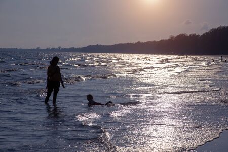 romantic silhouette mother and kid love together on ocean wave in sunset.の写真素材