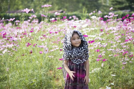 romantic moment of asian kid breezing on daisy flower agriculture field. Fashion action with natureの写真素材