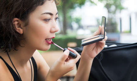 happy asian woman make up lips with gross lipstick in pink shade outdoor park background in banner sizeの写真素材