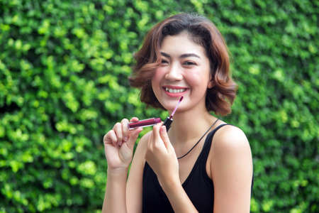 happy asian woaman make up lips with gross lipstick in pink shade outdoor park backgrpundの写真素材