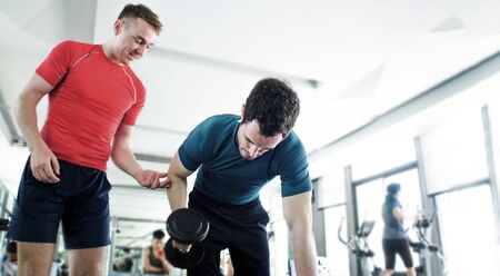 personal body building trainner at gym with dumbbell to making muscle and loss weight. Exercise need coach to support and teaching moving object and sport equipment on focus good shape.の写真素材