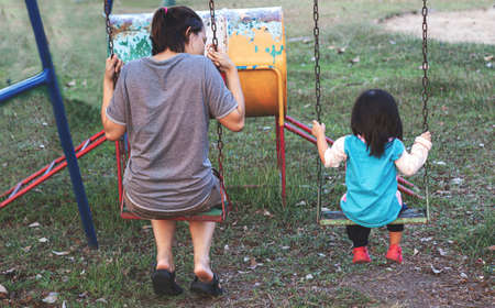 mother and kid talking on swing at play park in public placeの写真素材