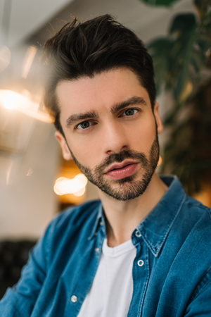Fashion portrait of a handsome bearded man with stylish haircut wearing trendy casual clothes sitting in beauty salon. Male model posing for pictures, he is good looking.の写真素材