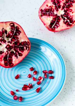 Red juicy pomegranate in the blue plate on the tableの写真素材