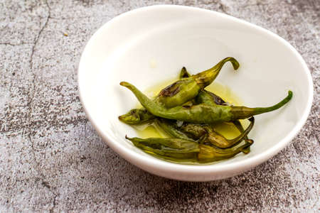 Roasted hot peppers in a white bowl with the marinadeの写真素材