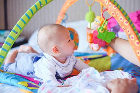 Cute little Asian 5 - 6 months old  baby boy child at tummy time on the play gym playing with his Daddy on Bed in Bedroom at Home - Selective Focusの写真素材