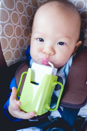 Cute little asian toddler baby boy drinking milk from a box with a straw in car seat  in carの写真素材