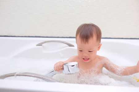 Cute little Asian 18 months / 1 year old toddler baby boy child having fun sitting in bathtub...