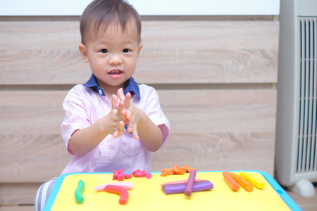 Cute smiling little Asian 18 months old toddler baby boy child having fun playing modeling clay / play dought at play school / child care, Montessori education Creative play for toddlers conceptの写真素材