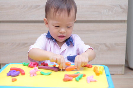 Cute smiling little Asian 18 months / 1 years old toddler boy child having fun playing modeling clay / play dought at home, Improve & Increase Concentration In Kids, Creative play for toddlers conceptの写真素材