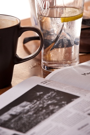 Reading newspaper in coffee-house during break. On the table glass of lemon water and coffee mug. In foreground newspaper.の写真素材